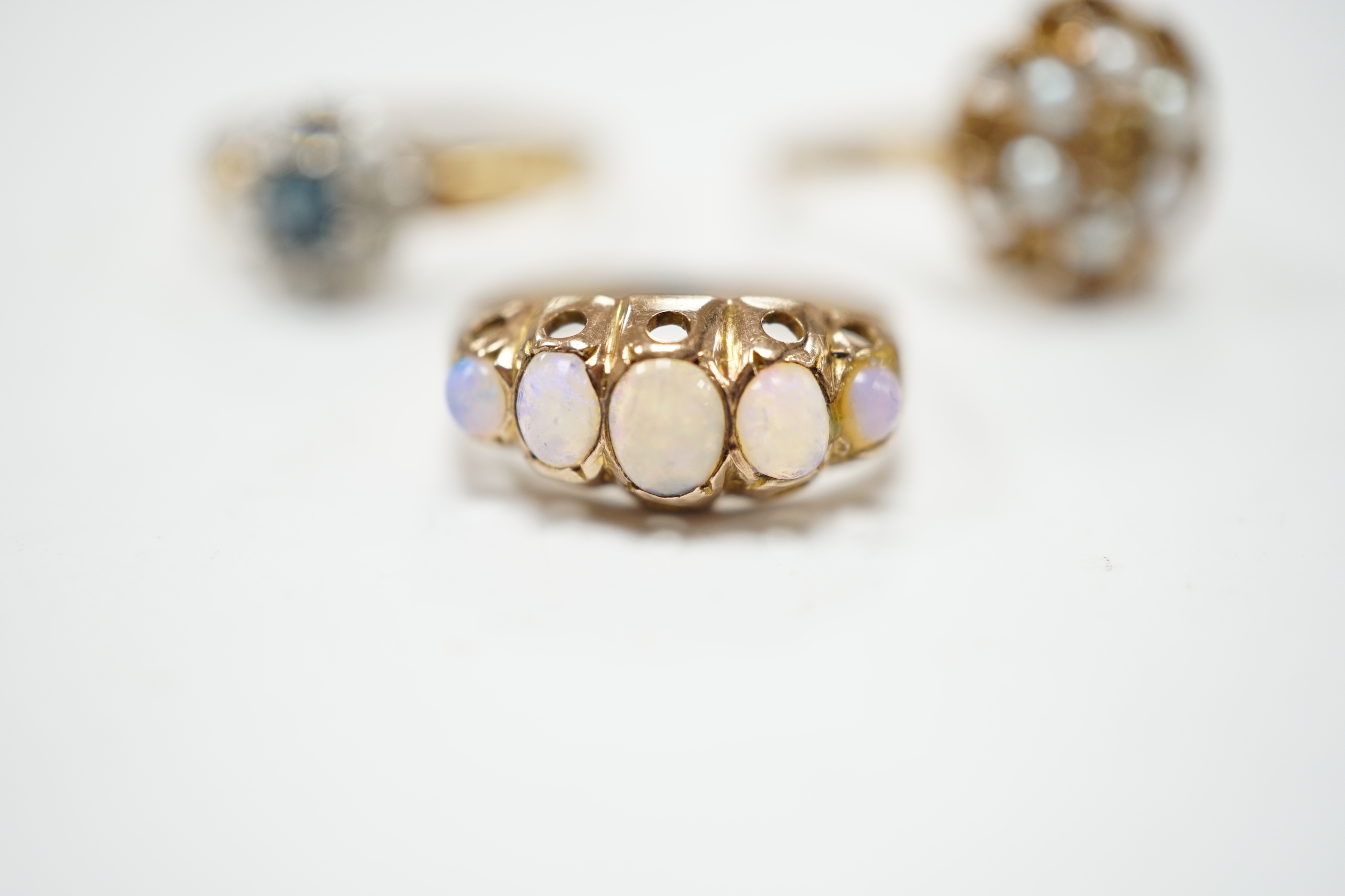 A late Victorian 9ct gold and graduated five stone opal set half hoop ring, size L, a 9ct, seed pearl and citrine cluster set flower head ring, gross 4.7 grams and a costume ring.